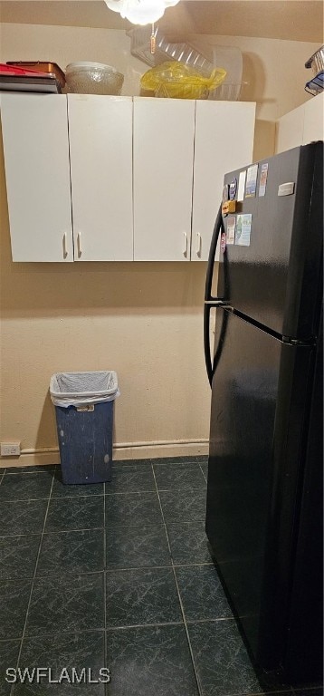 kitchen with dark tile patterned floors, black refrigerator, and white cabinetry