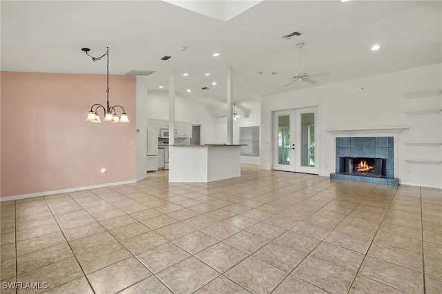 unfurnished living room featuring ceiling fan with notable chandelier, light tile patterned flooring, lofted ceiling, and a fireplace