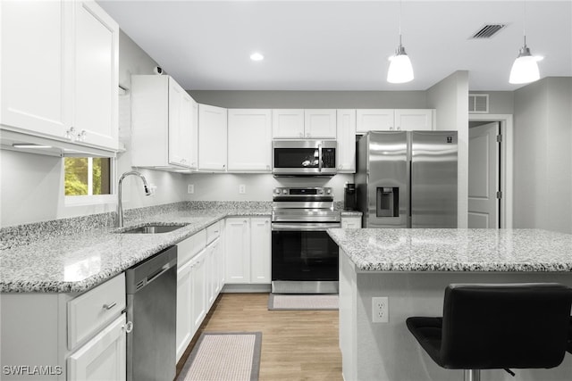 kitchen with appliances with stainless steel finishes, sink, white cabinets, a kitchen island, and hanging light fixtures