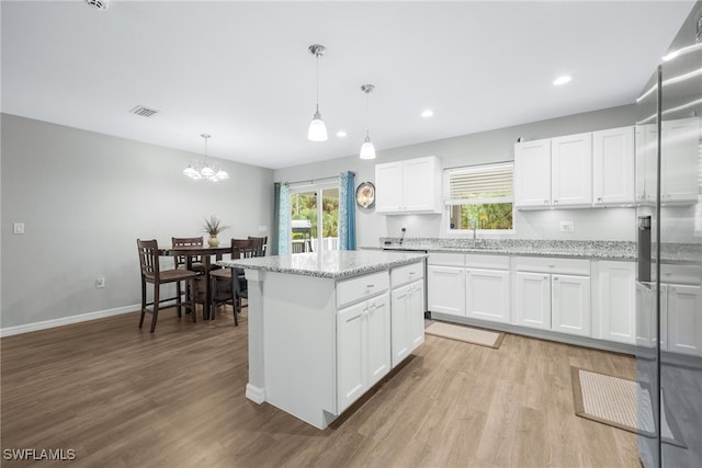 kitchen with light stone counters, a center island, white cabinets, and decorative light fixtures