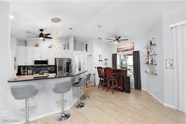 kitchen with stainless steel appliances, white cabinetry, backsplash, a breakfast bar, and ceiling fan