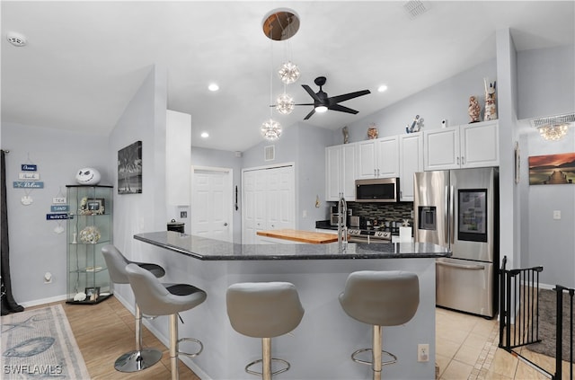 kitchen with kitchen peninsula, appliances with stainless steel finishes, ceiling fan, lofted ceiling, and white cabinets