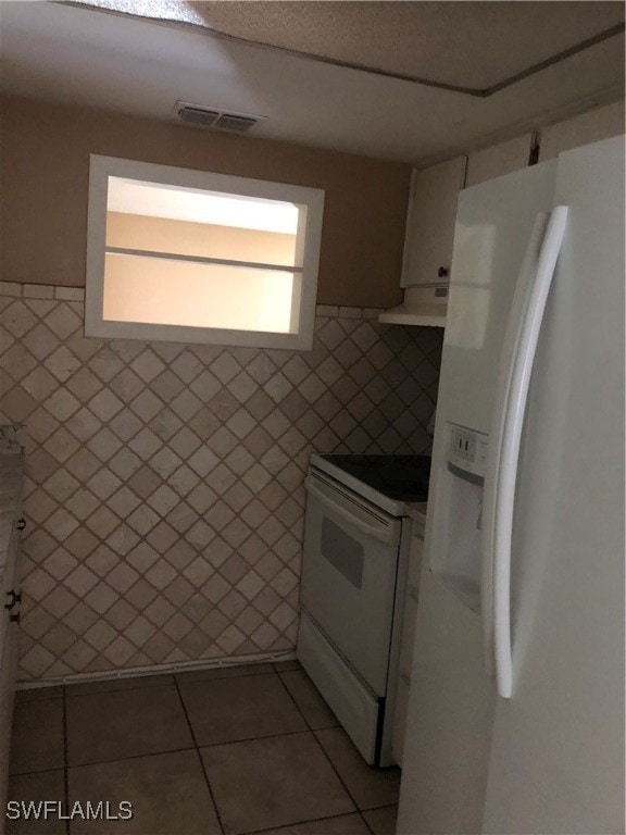 kitchen with dark tile patterned flooring, tile walls, white appliances, and extractor fan