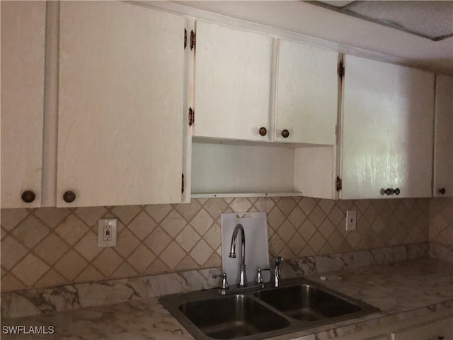 kitchen featuring light stone countertops, tasteful backsplash, sink, and white cabinets