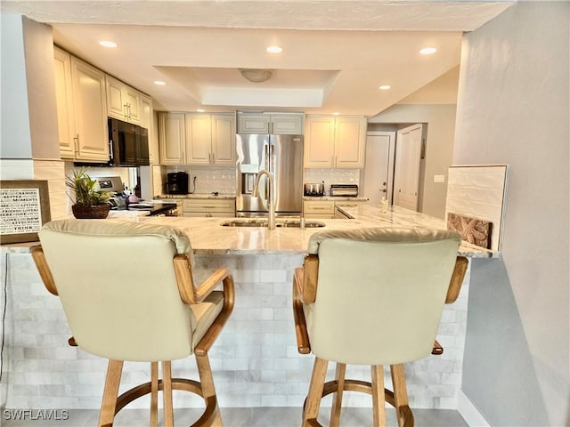 kitchen featuring a breakfast bar area, backsplash, a tray ceiling, stainless steel fridge with ice dispenser, and kitchen peninsula