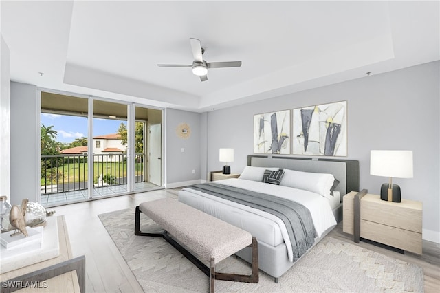 bedroom with a tray ceiling, access to exterior, light wood-type flooring, and ceiling fan