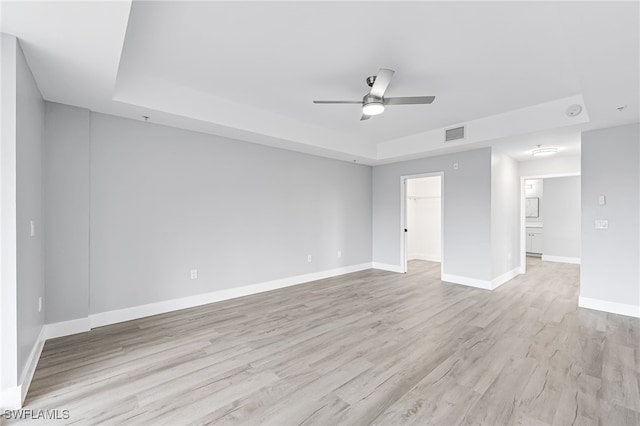 empty room with light hardwood / wood-style floors, a raised ceiling, and ceiling fan