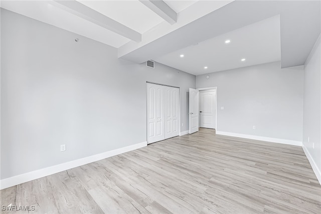 unfurnished bedroom featuring light hardwood / wood-style flooring, a closet, and beamed ceiling