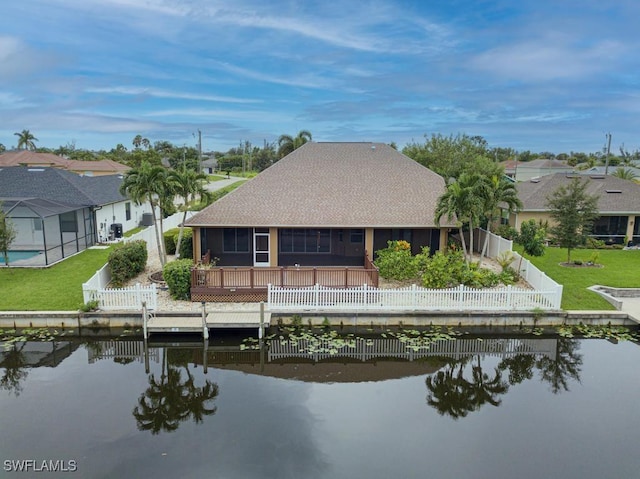 back of property featuring a sunroom, a water view, and a lawn