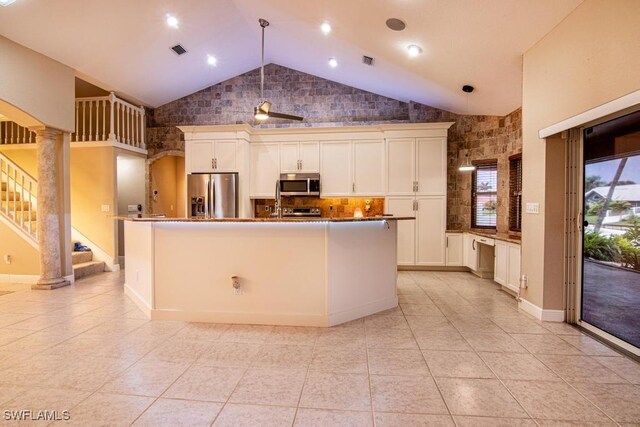 kitchen featuring ornate columns, stainless steel appliances, tasteful backsplash, pendant lighting, and a center island with sink