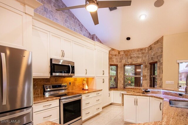 kitchen featuring lofted ceiling, decorative backsplash, light stone countertops, appliances with stainless steel finishes, and light tile patterned flooring