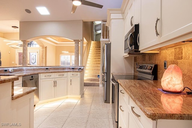 kitchen with light stone countertops, tasteful backsplash, decorative columns, stainless steel appliances, and white cabinetry