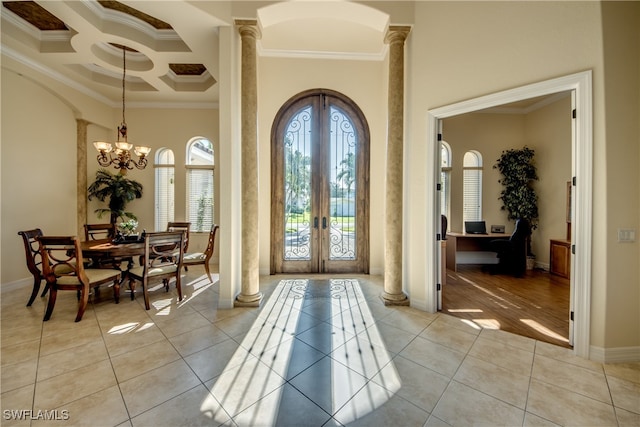 foyer featuring an inviting chandelier, french doors, light wood-type flooring, decorative columns, and ornamental molding