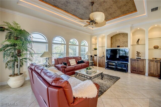 living room with a raised ceiling, light tile patterned floors, built in features, ornamental molding, and ceiling fan