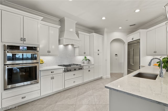 kitchen with premium range hood, light stone counters, stainless steel appliances, white cabinetry, and sink