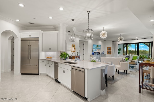 kitchen featuring hanging light fixtures, appliances with stainless steel finishes, open floor plan, white cabinetry, and a sink