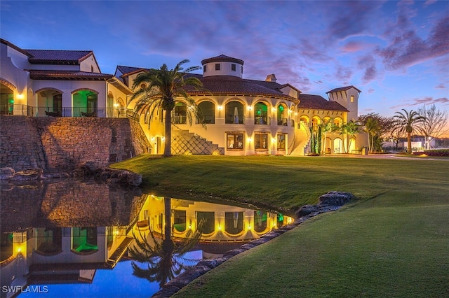 back of property at dusk with a yard and a tile roof