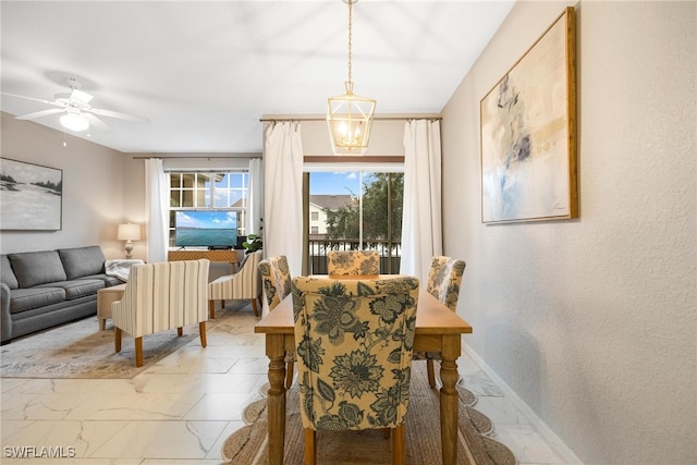 dining area featuring ceiling fan with notable chandelier, marble finish floor, and baseboards