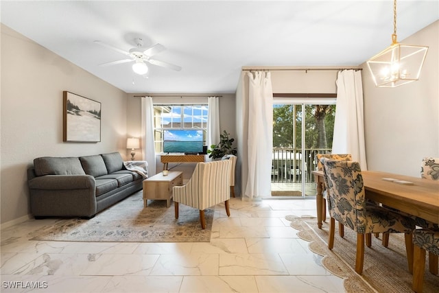 living area with ceiling fan with notable chandelier, marble finish floor, and baseboards