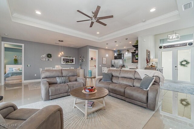 tiled living room featuring ceiling fan with notable chandelier, a tray ceiling, and ornamental molding