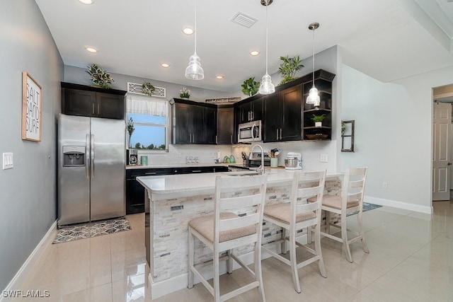 kitchen featuring appliances with stainless steel finishes, a kitchen breakfast bar, light stone counters, light tile patterned floors, and decorative light fixtures