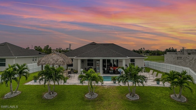 back house at dusk featuring a yard and a patio area