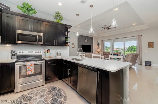 kitchen with sink, kitchen peninsula, hanging light fixtures, stainless steel appliances, and a raised ceiling