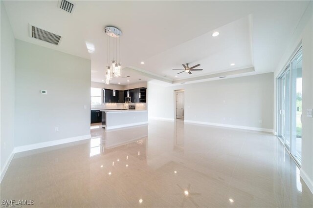 unfurnished living room featuring ceiling fan and a raised ceiling