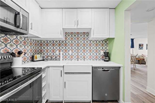 kitchen with appliances with stainless steel finishes, white cabinetry, tasteful backsplash, and light hardwood / wood-style floors