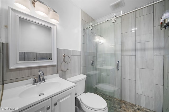 bathroom with tile walls, a shower with shower door, vanity, and toilet