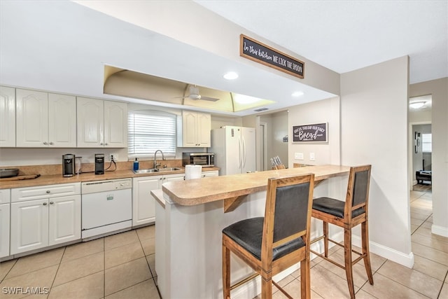 kitchen featuring a raised ceiling, a kitchen bar, white cabinetry, sink, and white appliances