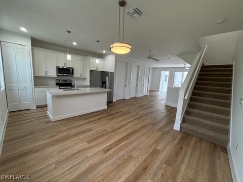 kitchen with visible vents, white cabinetry, open floor plan, appliances with stainless steel finishes, and a center island with sink