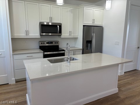 kitchen with wood finished floors, light countertops, stainless steel appliances, white cabinetry, and a sink