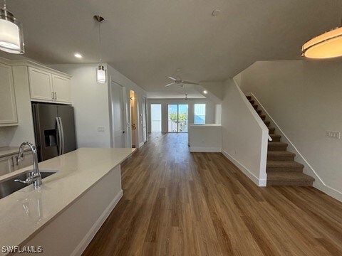 kitchen featuring wood finished floors, a sink, white cabinetry, light countertops, and stainless steel refrigerator with ice dispenser