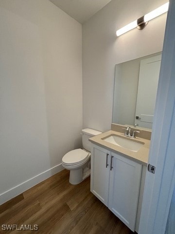 half bathroom with toilet, wood finished floors, vanity, and baseboards