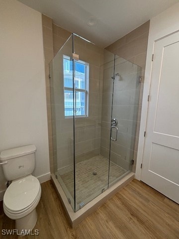 bathroom featuring a stall shower, wood finished floors, toilet, and baseboards