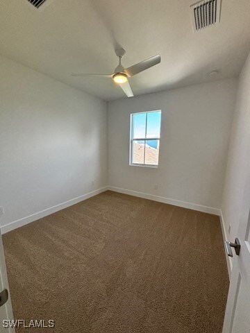 carpeted spare room with baseboards, visible vents, and a ceiling fan