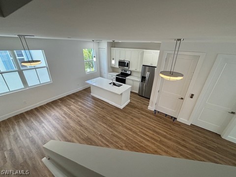 kitchen with sink, a kitchen island with sink, dark wood-type flooring, and stainless steel appliances