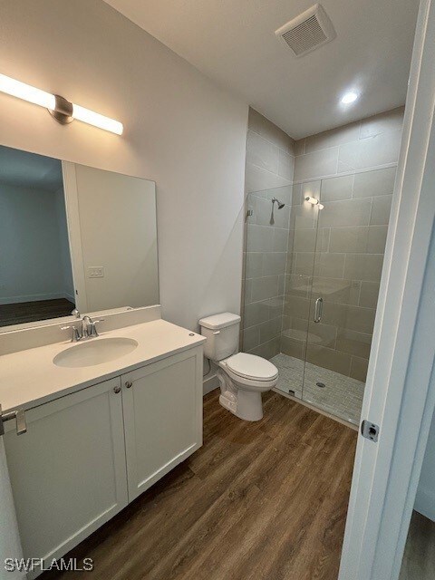 bathroom with a shower with door, toilet, vanity, and wood-type flooring