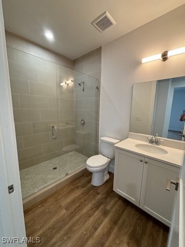 bathroom featuring toilet, wood-type flooring, a shower with door, and vanity