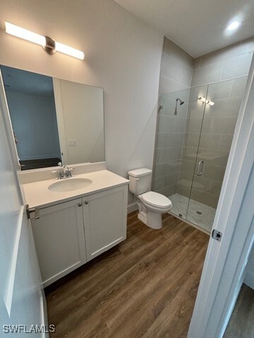 bathroom featuring hardwood / wood-style floors, a shower with door, toilet, and vanity