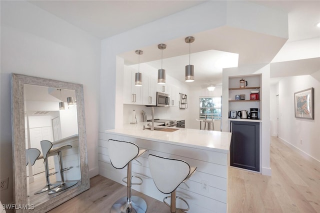 kitchen featuring kitchen peninsula, light hardwood / wood-style flooring, white cabinets, hanging light fixtures, and a breakfast bar area