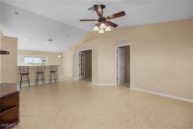 empty room featuring ceiling fan, bar, vaulted ceiling, and light tile patterned flooring