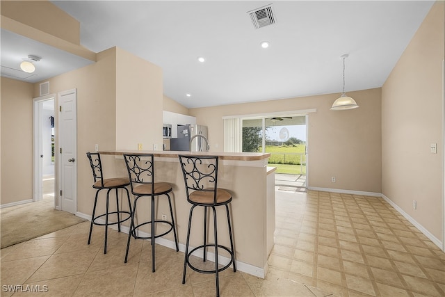 kitchen featuring a kitchen bar, vaulted ceiling, kitchen peninsula, hanging light fixtures, and appliances with stainless steel finishes