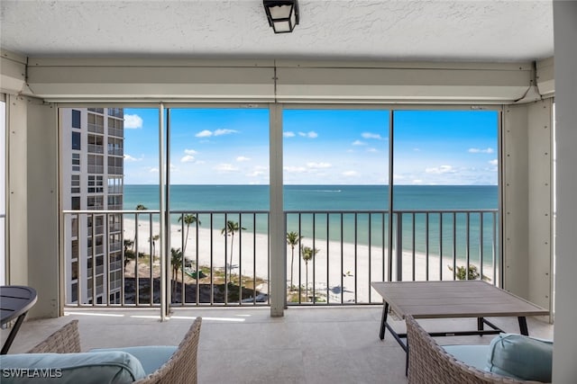 sunroom / solarium with a beach view, a water view, and a wealth of natural light