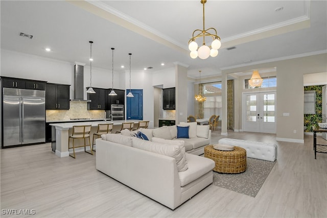 living room featuring a notable chandelier, a raised ceiling, french doors, and crown molding