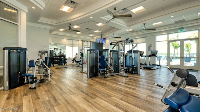 gym featuring a tray ceiling, light hardwood / wood-style flooring, ceiling fan, and french doors