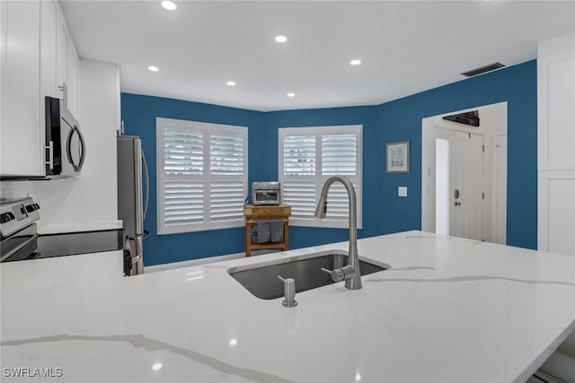 kitchen with a sink, white cabinetry, recessed lighting, stainless steel appliances, and light stone countertops