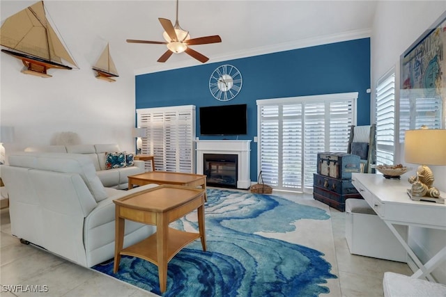 living area with tile patterned floors, a glass covered fireplace, ceiling fan, and ornamental molding