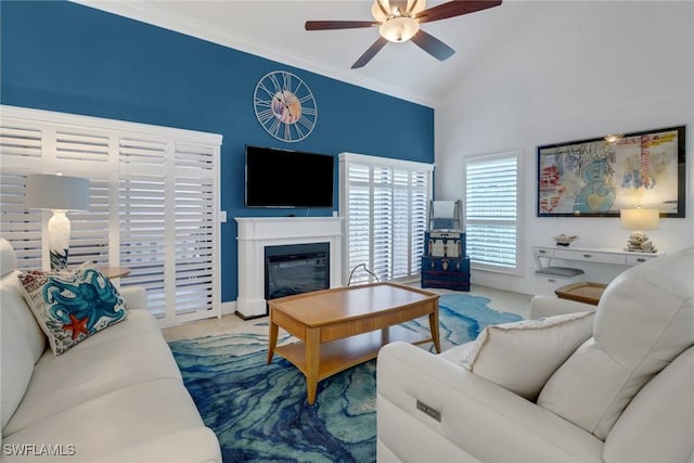 living area featuring high vaulted ceiling, ornamental molding, a glass covered fireplace, baseboards, and ceiling fan